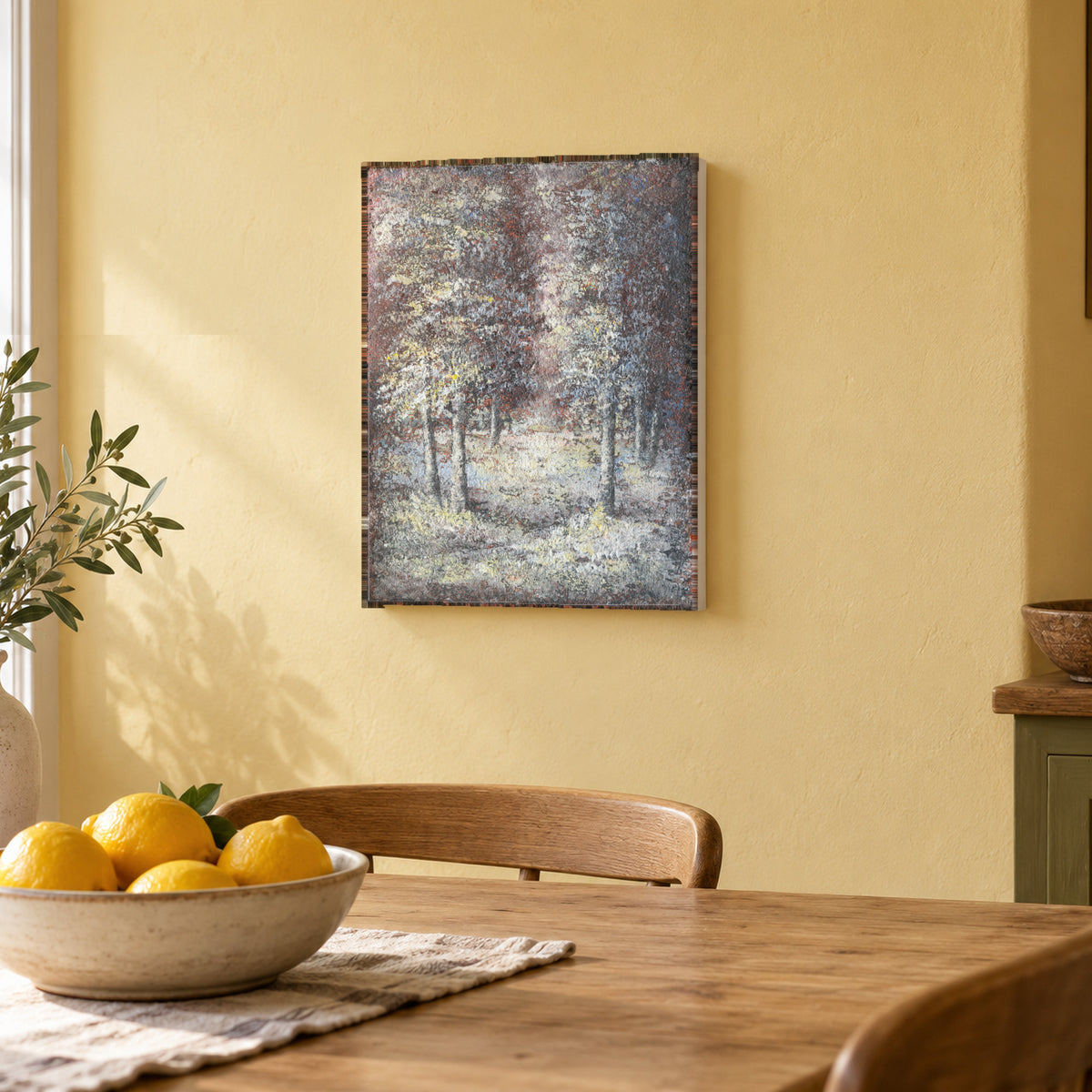 Winter Grove by Yingzhi Chen hanging on a pale butter-yellow plaster wall above a light wood dining table edge with a bowl of lemons