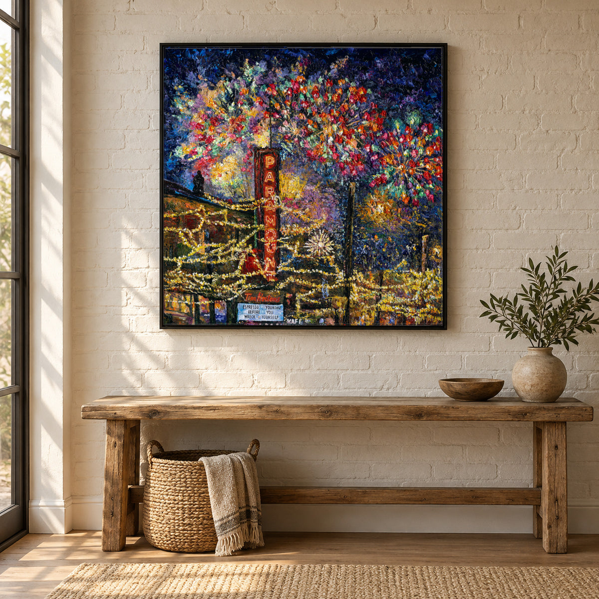 Downtown Kelowna, Fireworks by Zhongda Huang hanging on a warm white brick wall painted white above a rustic pine bench with a woven basket